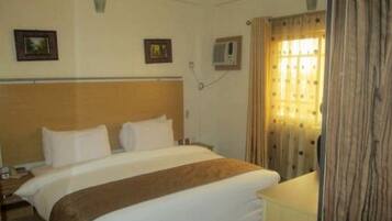 Habitación de hotel con cama, mesita de noche, lámpara y ventana con cortinas.
