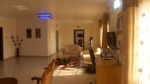A living room with a sofa, a dining table, and a TV. There is a vase with flowers on the left and a window on the right. - Room-ayalla Hotel-superior Deluxe (Port Harcourt)