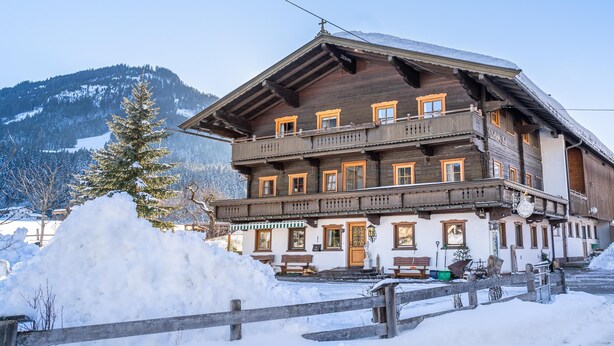 A two-story wooden building with balconies, a wooden fence, and a snow-covered ground. - Holiday home on a former stables (Brixen im Thale)