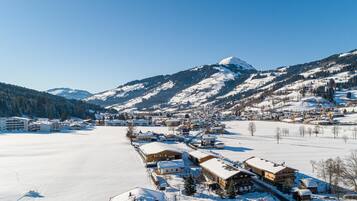 A snow-covered village with buildings along a frozen lake, surrounded by mountains.