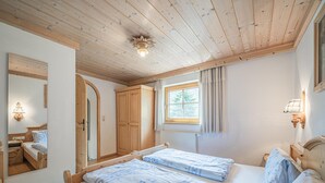 A bedroom with two beds, wooden ceiling, a window with curtains, and a mirror. - Holiday home on a former stables (Brixen im Thale)