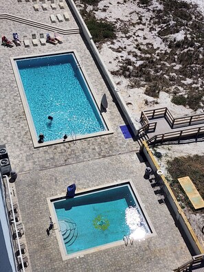 Dos piscinas rectangulares con agua cristalina, rodeadas de sillas de descanso y una terraza de madera.