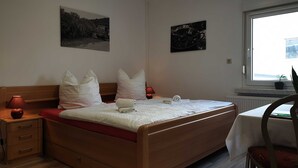Ein ordentlich bezogenes Bett mit Kissen, ein Nachttisch mit Lampe sowie zwei an der Wand hängende Bilder.