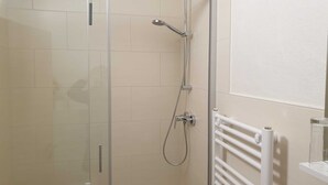 Eine gläserne Dusche mit Handbrause und am Wand montierter Armatur.