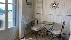 Ein Zimmer mit Tisch, Stühlen, einem Ventilator, einem Fenster mit Vorhängen, einem Bild an der Wand und einer Sonnendekoration.