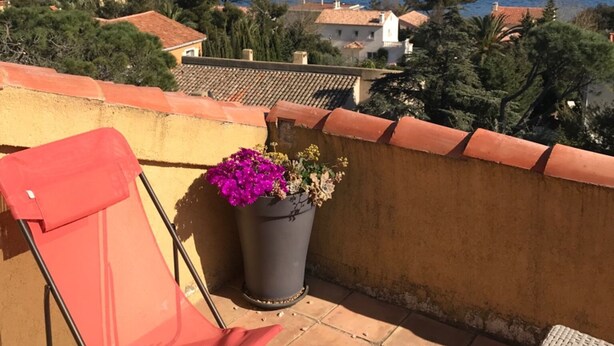 Ein Balkon mit einem roten Stuhl, einem Topfpflanzen und Blick auf das Meer und Gebäude.