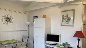 Ein gemütlicher Wohnbereich mit einem weißen Schrank, einem Flachbildfernseher, einer Lampe und einem kleinen Tisch mit einem Gesellschaftsspiel.