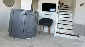 Ein Zimmer mit einem grauen Schrank, einem schwarzen Stuhl, einem an der Wand montierten Fernseher und einer Treppe mit Glasgeländer.