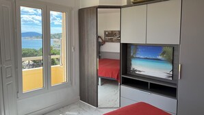 Ein Schlafzimmer mit großem Fenster, einem Bett mit roter Bettdecke, einem Fernseher und einem Kleiderschrank.