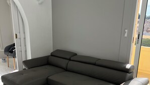 Ein modulares Sofa in einem modernen Raum mit weißem Marmorboden, einer weißen Wand und Blick durch eine Glastür.