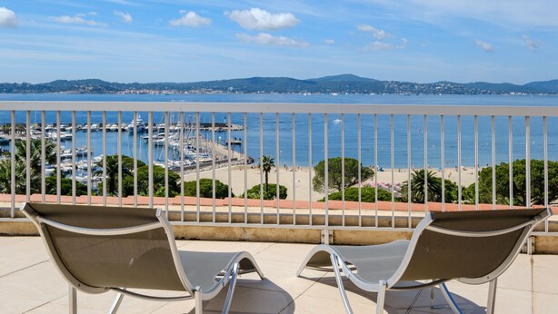 Ein Balkon mit zwei Stühlen mit Blick auf einen Jachthafen und einen Strand.