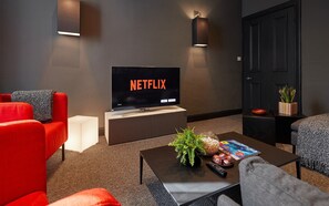 A modern living room with a flat-screen TV displaying 'NETFLIX', a sofa, a coffee table with a plant, a remote, and a magazine.