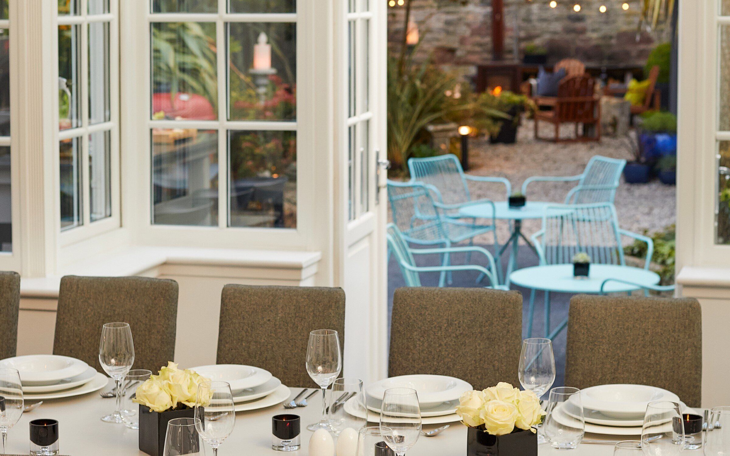 A dining area with tables set for a meal, chairs, and a view of the outdoor seating area through large windows.