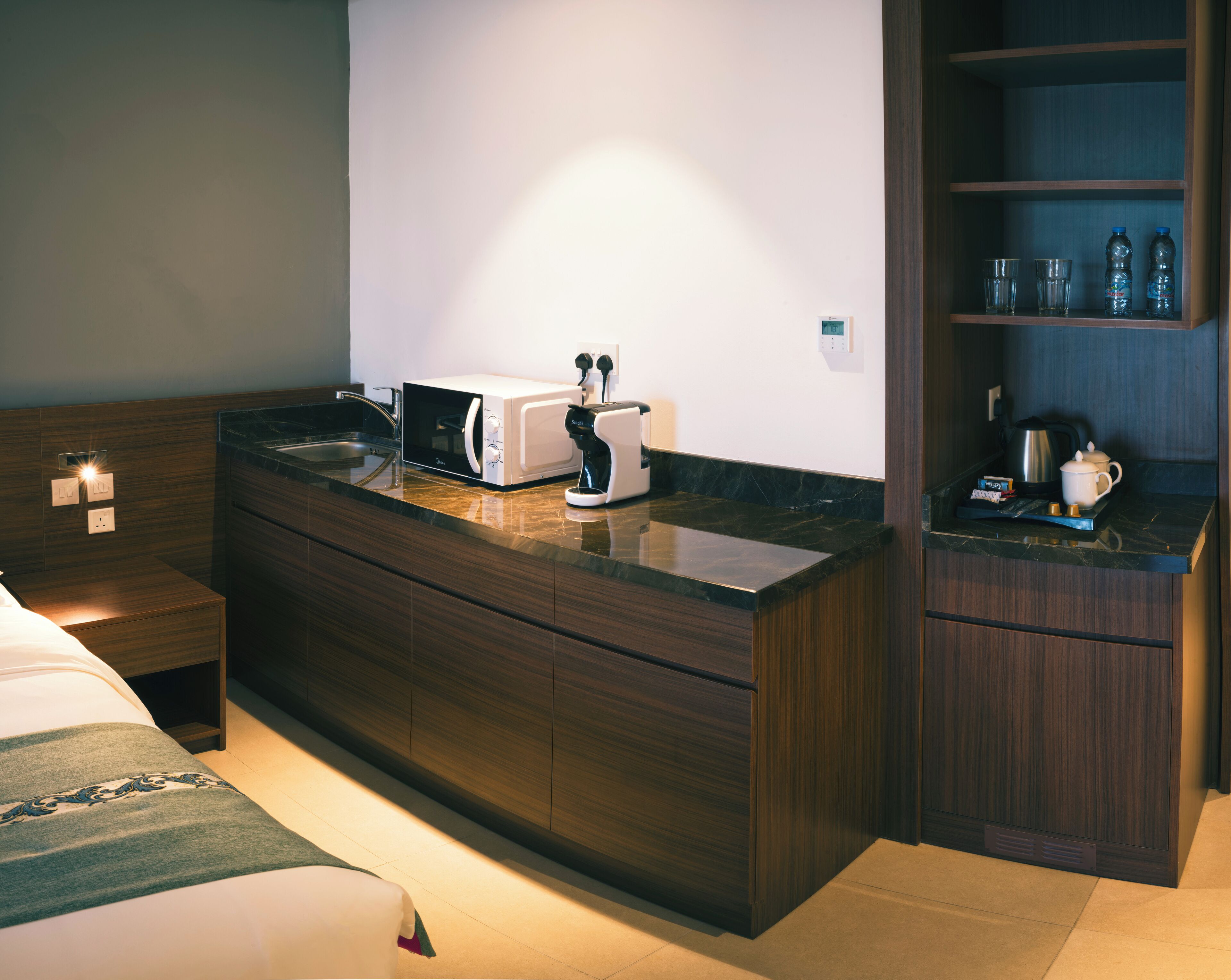 Une chambre d’hôtel moderne équipée d’une coiffeuse en bois, d’un four à micro-ondes et d’une machine à café.