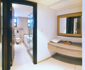 A modern bathroom with a glass shower enclosure, a white toilet, and a vanity with a gold-framed mirror. - Boulevard hotel (Seeb)