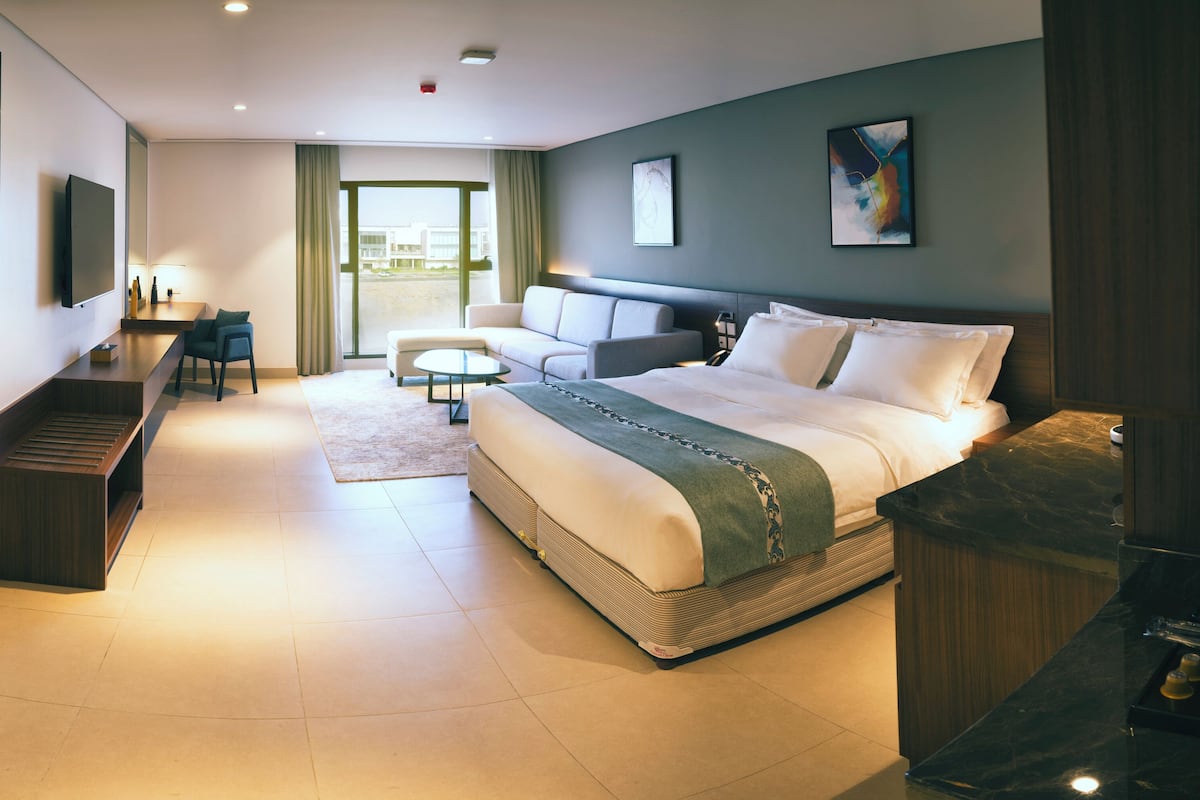 A modern hotel room with a large bed, a sofa, a desk, and a TV.