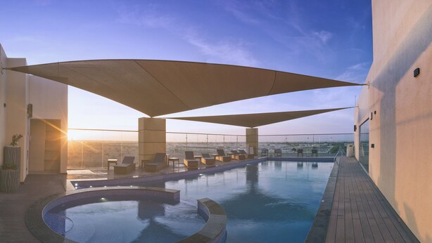 A rooftop infinity pool with sun loungers and a view of the cityscape. - Boulevard hotel (Seeb)
