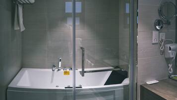 A modern bathroom with a glass-enclosed bathtub, a handheld showerhead, and a built-in toilet.