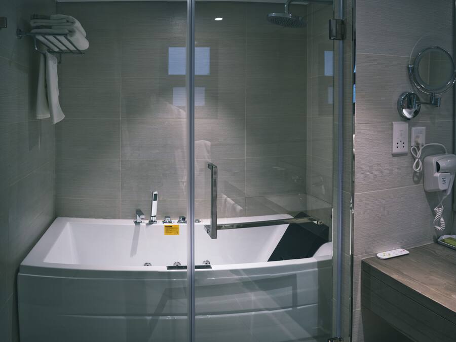 A modern bathroom with a glass-enclosed bathtub, a handheld showerhead, and a built-in toilet.