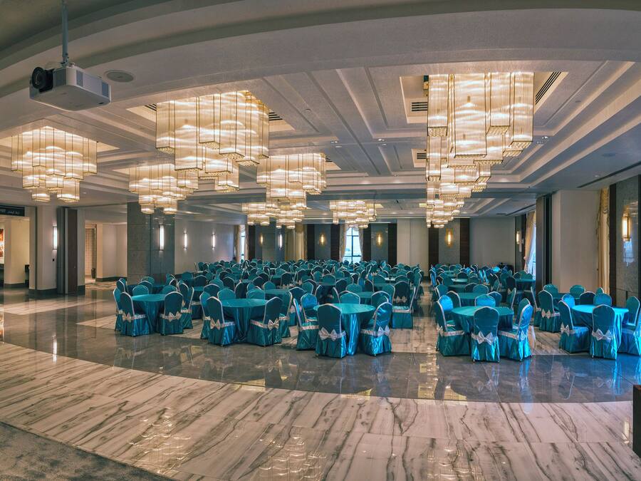 Un amplio salón de conferencias con filas de mesas y sillas, piso de mármol y modernos candelabros.