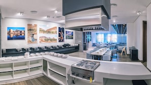 A modern kitchen with a built-in stove, white cabinetry, and a dining area with tables and chairs. - Boulevard hotel (Seeb)