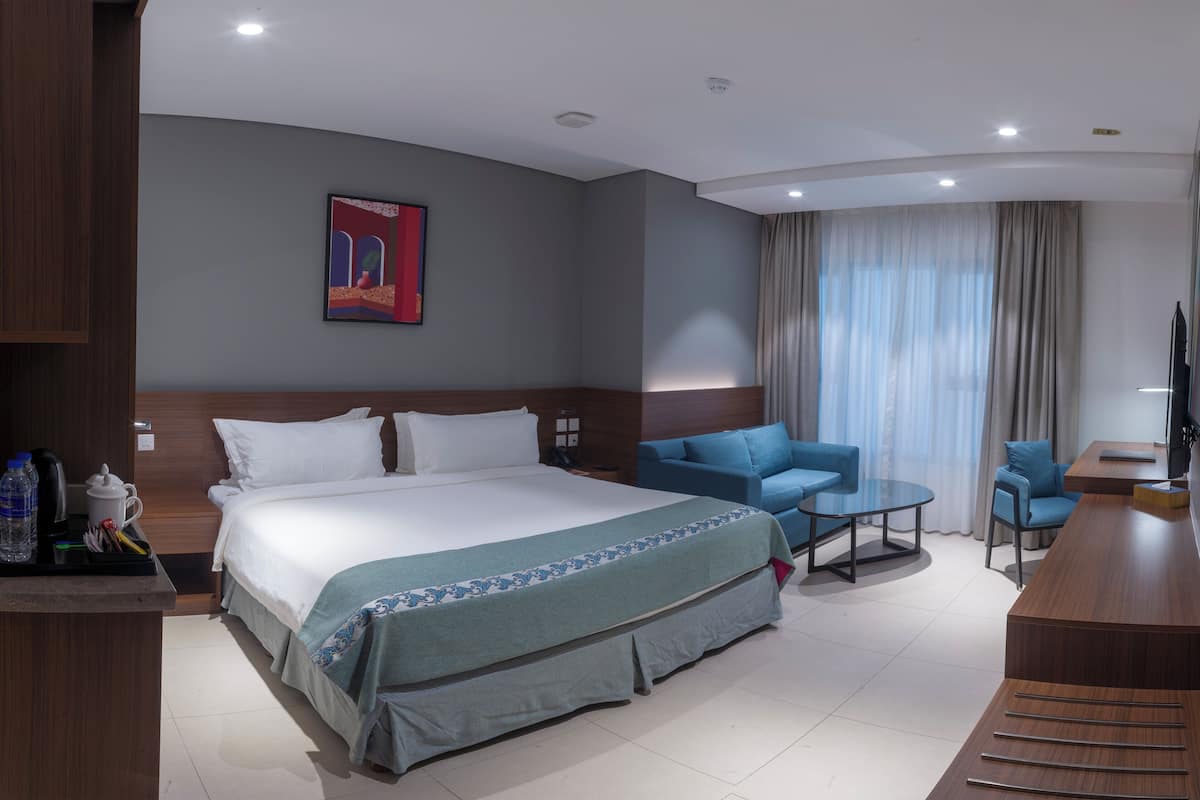 A modern hotel room with a large bed, a sofa, a desk, and a TV.
