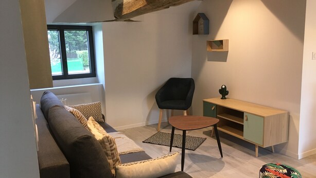 Un salon moderne avec un canapé, un fauteuil noir, une petite table en bois et un meuble.