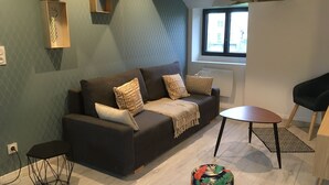 Un salon moderne avec un canapé marron foncé, des coussins à motifs, une petite table ronde et un pouf coloré.