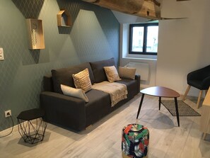Un salon moderne avec un canapé marron foncé, des coussins à motifs, une petite table ronde et un pouf coloré.