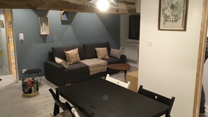 Un salon moderne avec un canapé foncé, des coussins à motifs, une petite table ronde et une table à manger avec des chaises.