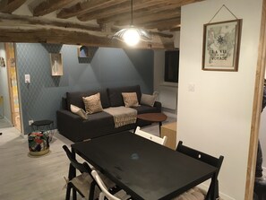 Un salon moderne avec un canapé foncé, des coussins à motifs, une petite table ronde et une table à manger avec des chaises.