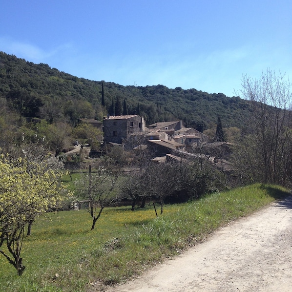A rural village with traditional stone buildings, a dirt road, and a hillside in the background.