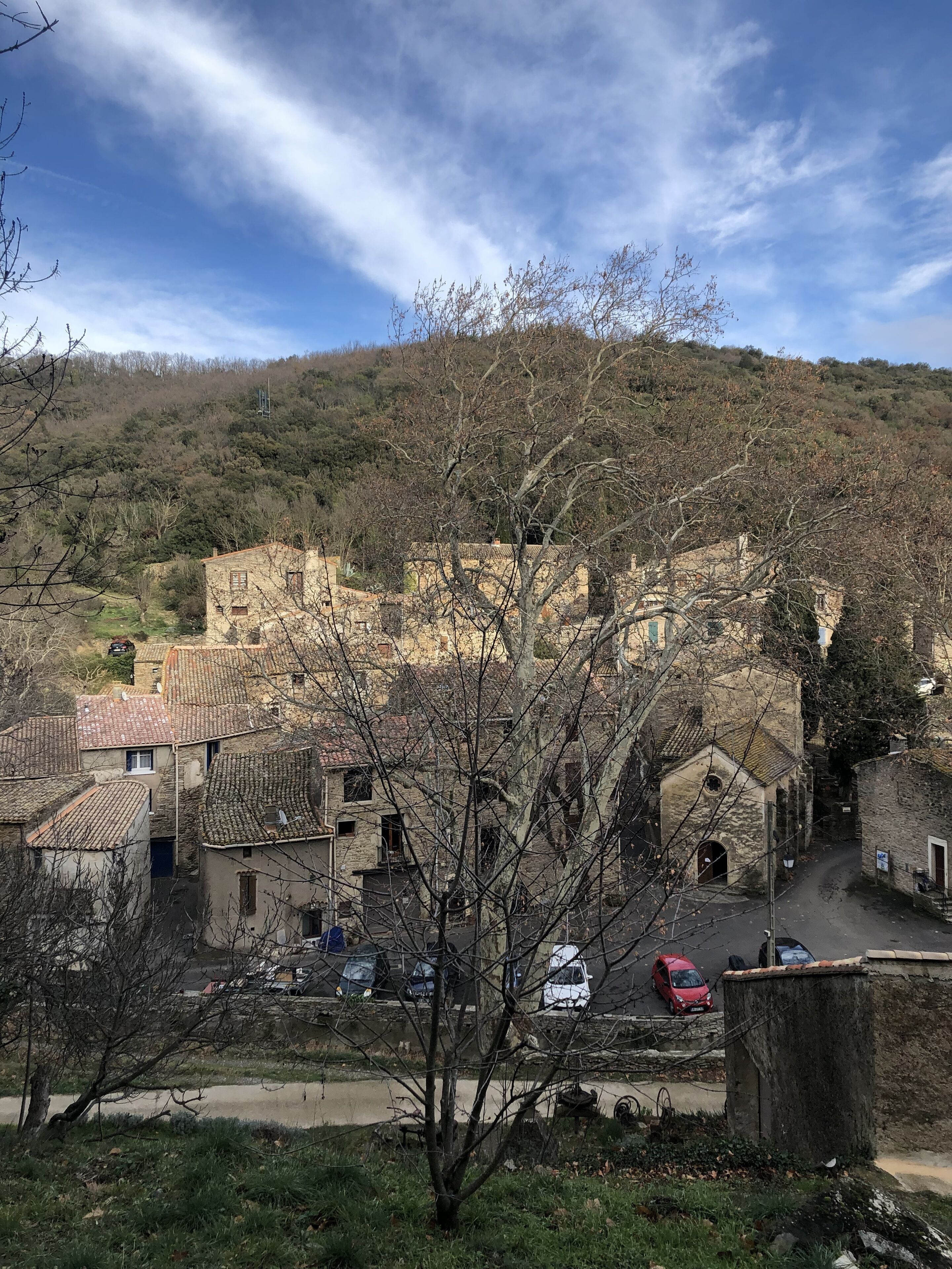 Un borgo collinare con edifici in pietra, strette vie e auto parcheggiate.
