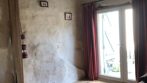 Une pièce dotée d’un plancher en bois, d’une grande fenêtre ornée de rideaux rouges et d’un mur sur lequel est accroché un seul tableau encadré.