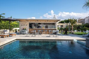 Uma área de bar moderna ao ar livre, com piscina, balcão de bar e assentos.