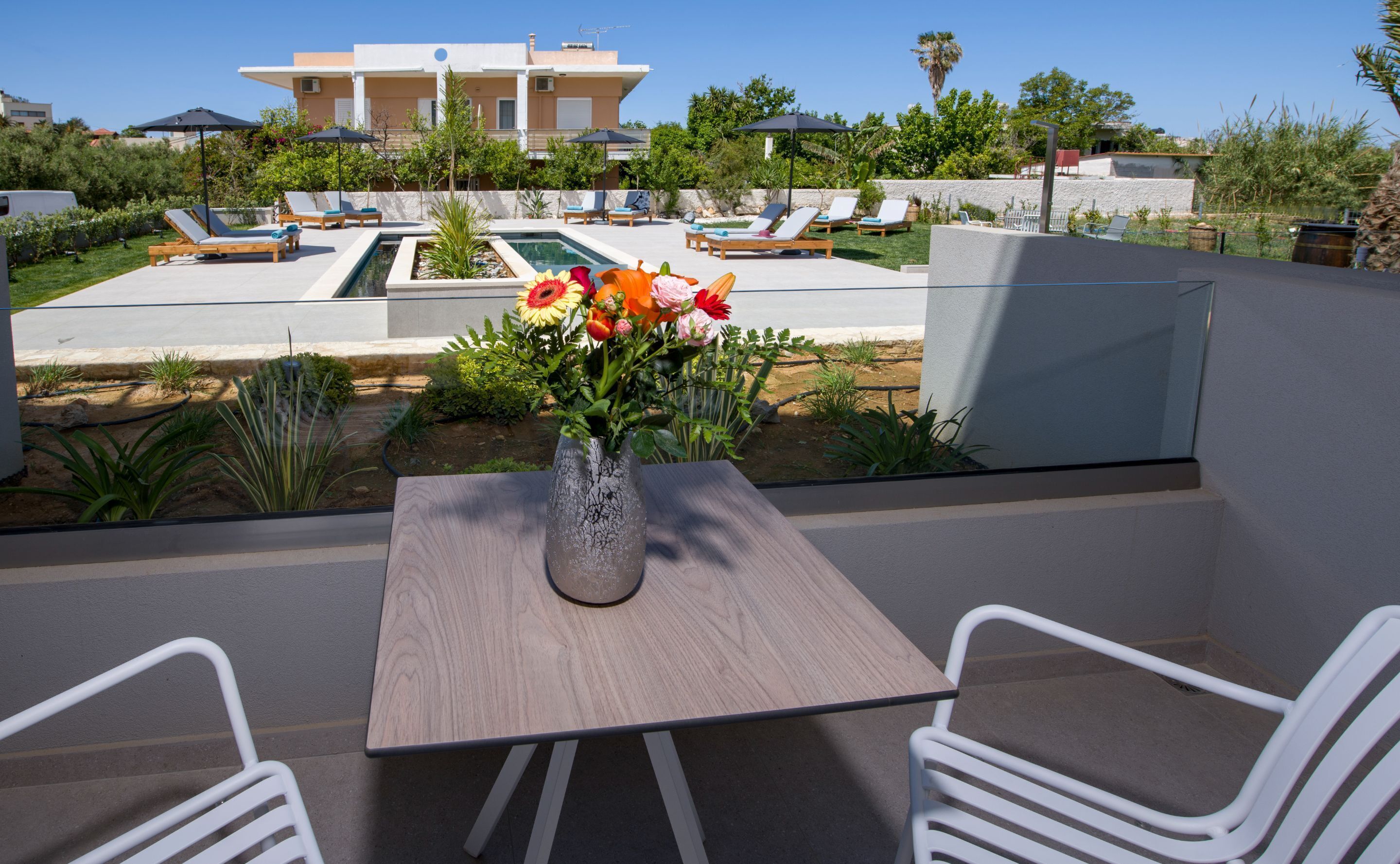 A modern outdoor seating area with a table and chairs, a pool, and a view of a building in the background.
