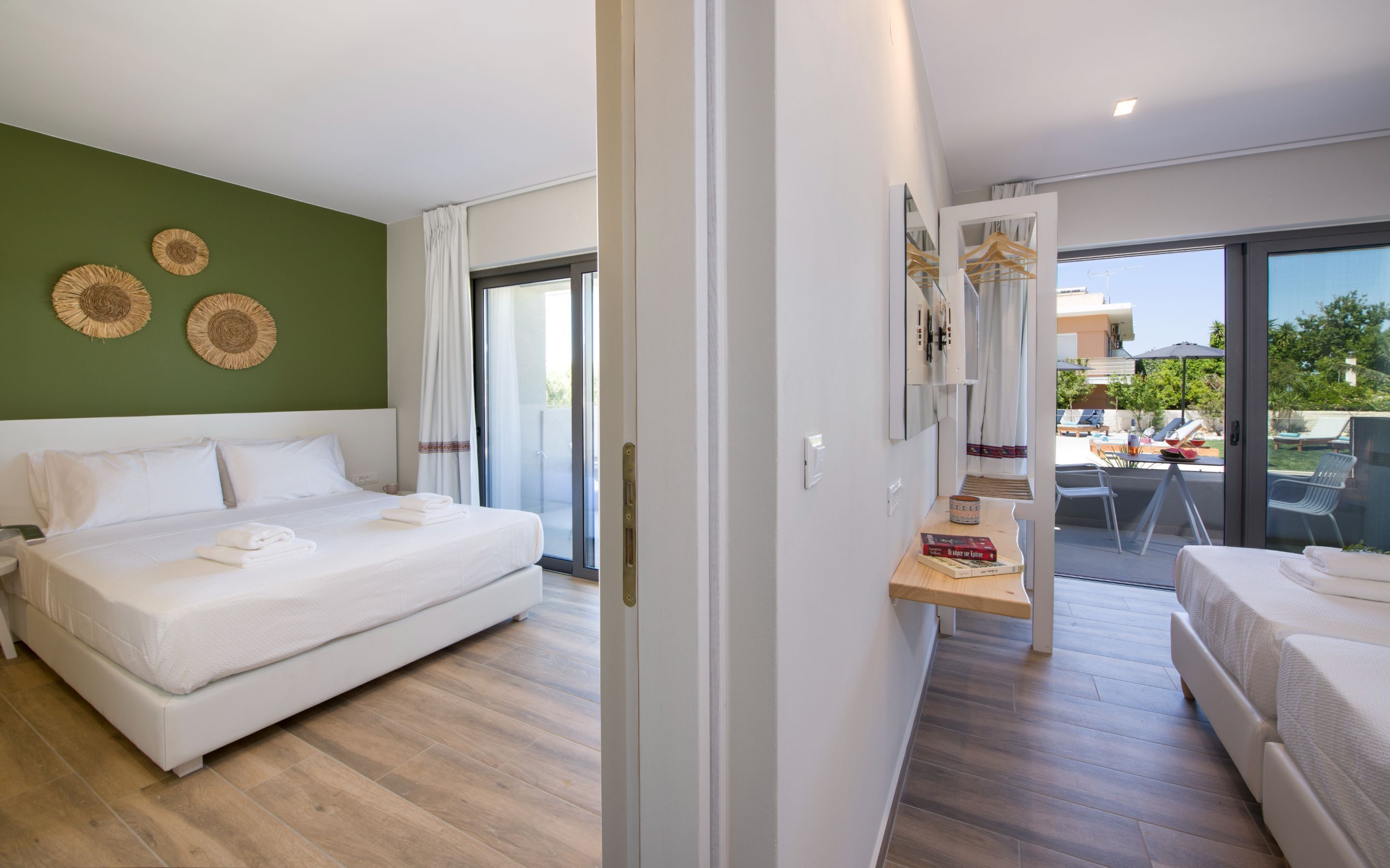 Une chambre d’hôtel moderne dotée d’un grand lit, d’un balcon avec vue et d’un coin repas visible à travers les portes vitrées.