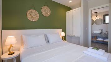 A hotel room with a large bed, two bedside lamps, a green accent wall, and a bathroom visible through an open door.