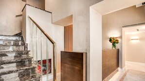Un interior moderno con una escalera de mármol, un revestimiento de madera y un mostrador de recepción con un florero.