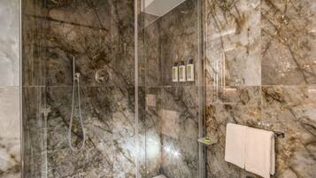 Ein modernes Badezimmer mit einer gläsernen Dusche, Marmorwänden, einem weißen Waschbecken und einem Handtuchhalter.