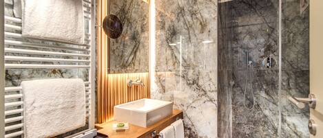 A modern bathroom with a marble shower, a wooden vanity, and a large mirror.