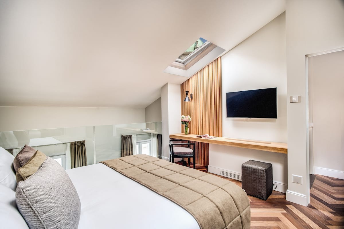 Een moderne hotelkamer met een groot bed, een bureau met stoel, een flatscreen televisie en een kleine prullenbak.