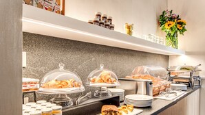 Disposición de un bufé con diversos alimentos, incluyendo pasteles y pan, además de salsas y condimentos sobre una encimera de granito.