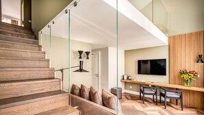Un interior moderno con una escalera de madera, un sofá con cojines, una zona de comedor con sillas y un televisor montado en la pared.