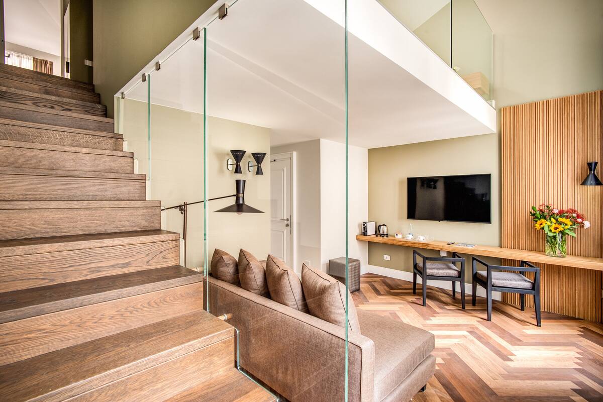 Een modern interieur met een houten trap, een bank met kussens, een eethoek met stoelen en een aan de muur bevestigde televisie.