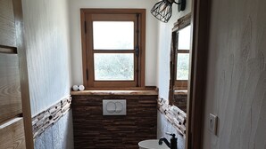 Un baño estrecho con tocador de madera, inodoro blanco y ventana sobre el lavabo.