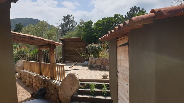 Un espacio al aire libre rústico con una pérgola de madera, escalones de piedra y un pequeño jardín.