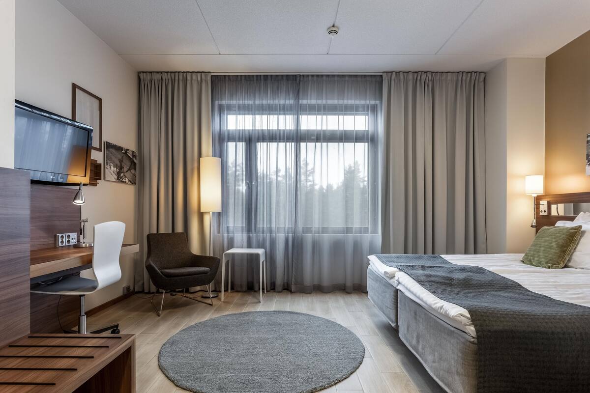 Ein Hotelzimmer mit Bett, Schreibtisch, Stuhl, Fernseher und Vorhängen.