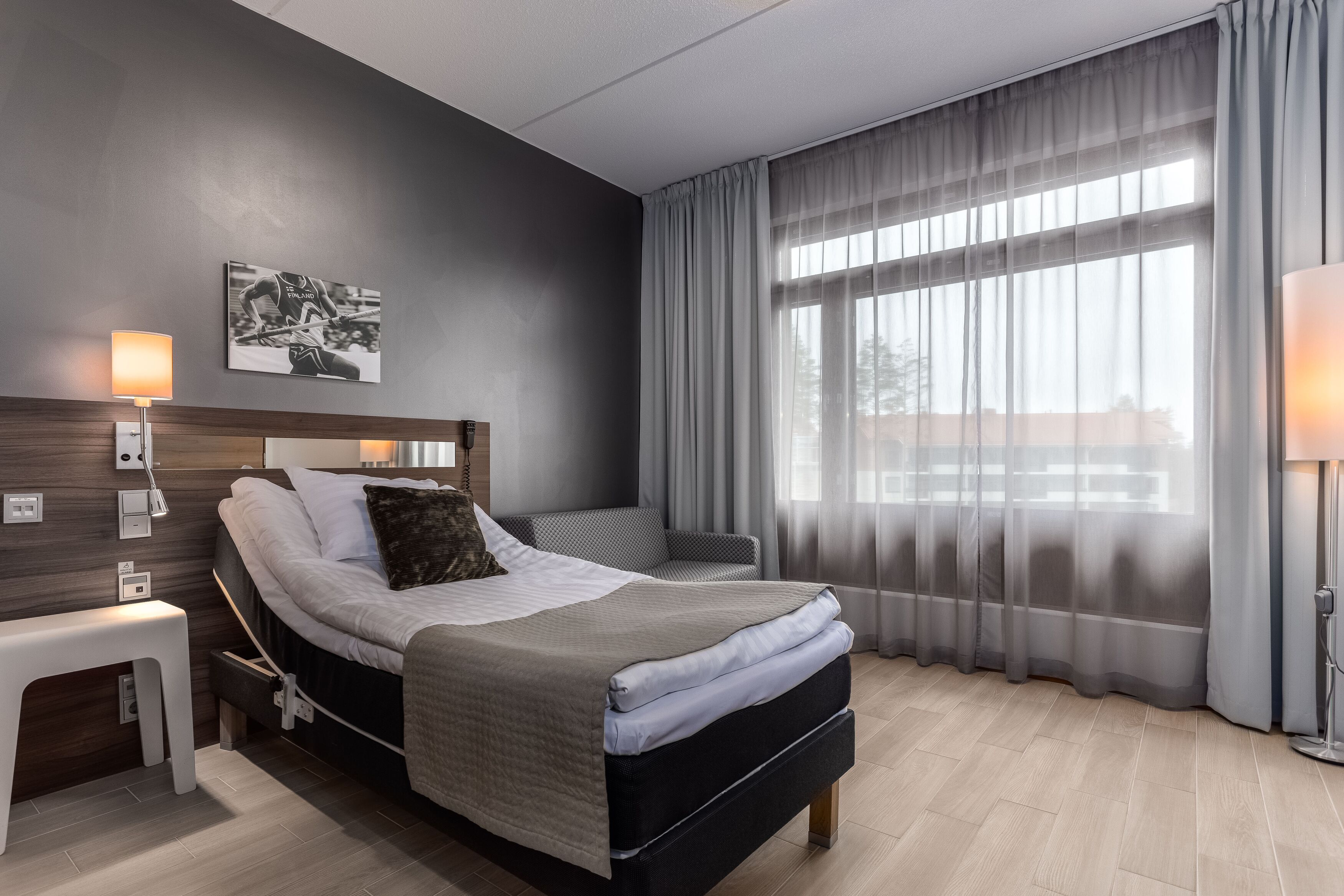 A modern bedroom with a bed, bedside table, lamp, and a large window with curtains.