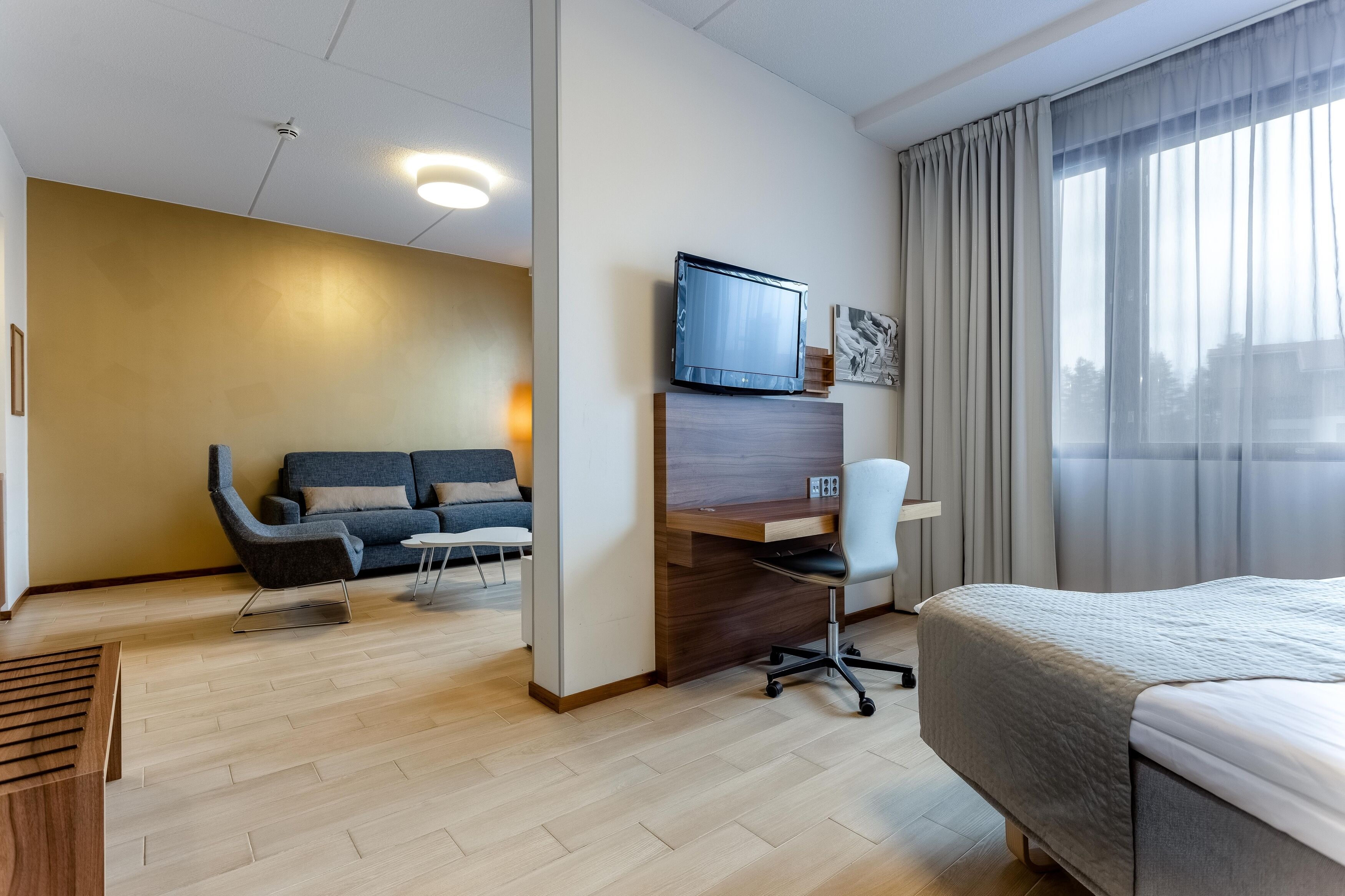 Una habitación de hotel con cama, escritorio, sillón, sofá y televisión.